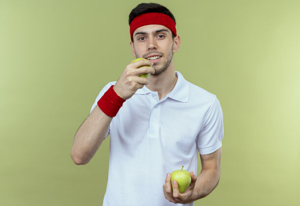 年轻戴着头巾的年轻人拿着绿色的苹果咬着绿色的苹果抱着运动头带
