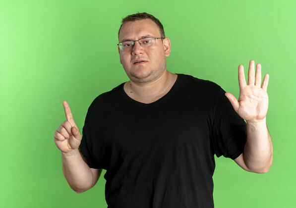 穿戴眼镜的超重男子身穿黑色t恤 手指指向绿色上方的第六根手指男士站立绿色
