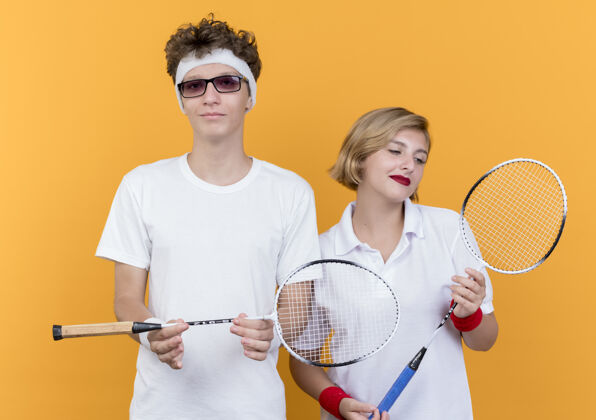 女人一对年轻的运动男女拿着球拍打网球 自信地微笑着越过橘子抱着运动球拍