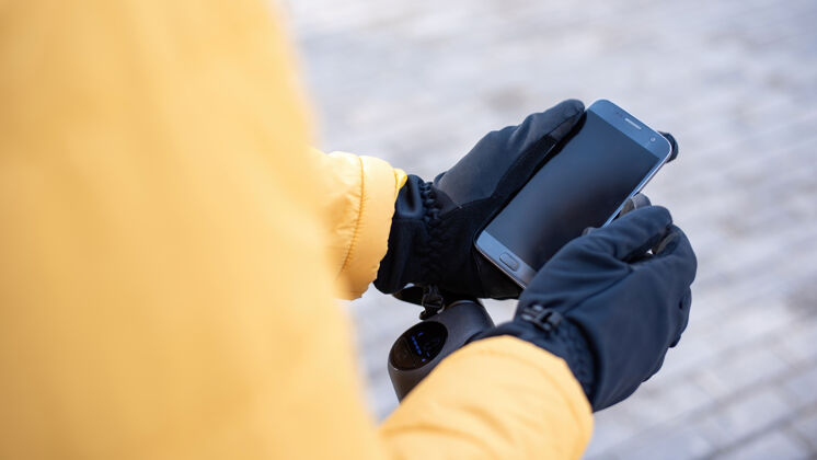 日常生活送食物的人骑着滑板车用他的智能手机黄色夹克和黑色手套冬天街道交通食品送货