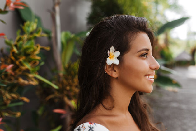 户外照片中 一位皮肤黝黑 头发花白的年轻女性正对着热带植物的墙壁摆姿势快乐人肖像