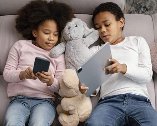 房子兄弟姐妹在家使用平板电脑和手机女孩设备兄弟姐妹
