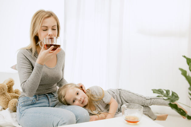 可爱阳光明媚的早晨 年轻的母亲和她的小女儿在家里喝酒茶亲吻