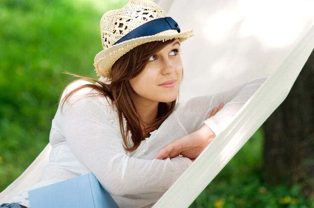 放松年轻女人拿着书在吊床上放松吊床休息休闲活动
