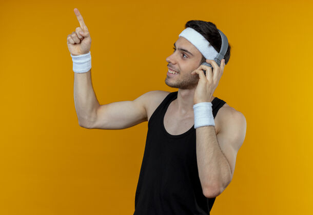 运动戴着头戴式耳机的年轻运动型男子一边看一边用手指指着橙色微笑指着头带向上