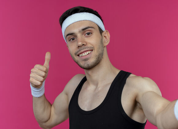 粉红戴着头巾的年轻运动型男子露出拇指 微笑着越过粉色男人运动微笑