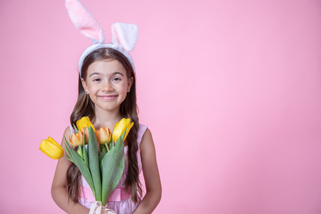 耳朵一个快乐的小女孩 带着复活节兔子耳朵 微笑着 手里拿着一束郁金香 站在粉色的画室里节日复活节兔子