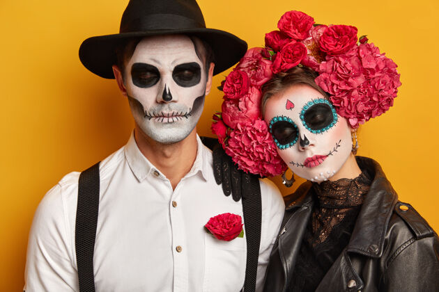 墨西哥冷静放松的情侣们准备好了流行的狂欢节 涂上诡异的妆容 闭上眼睛站在黄色背景下皮革庆祝服装