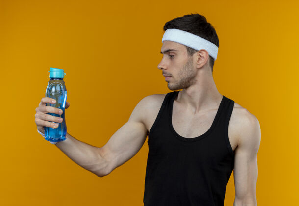 脸戴着头巾的年轻人拿着一瓶水 严肃地看着它站在橘色的墙上站着运动严肃
