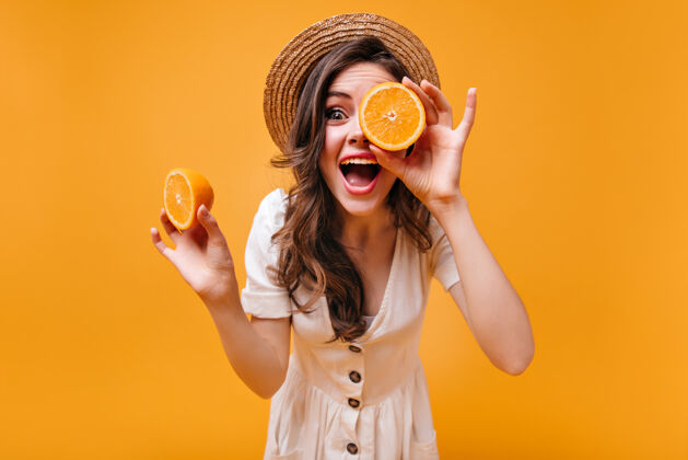 成人穿着棉衣 戴着草帽的女孩正和橘子在一个孤立的背景下嬉戏橙色水果橙色背景