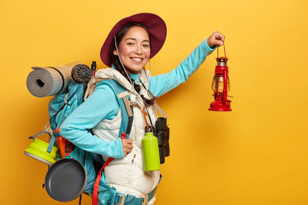 积极快乐的女旅行者拿着小灯摆姿势 准备探索未知的地方 精神高昂 肩上背着大背包 隔离在黄色的背景上姿势人个人