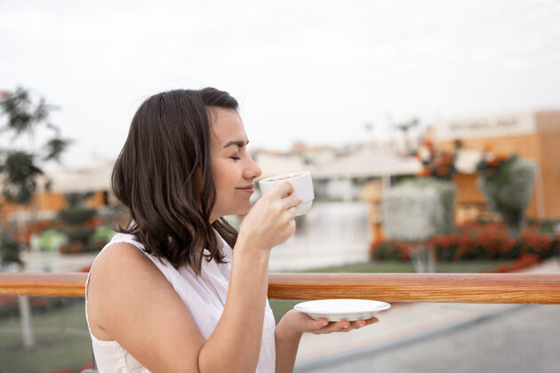 享受迷人的年轻女子手里拿着一杯咖啡和一个茶托 在户外享受早晨的时光年轻早晨休息