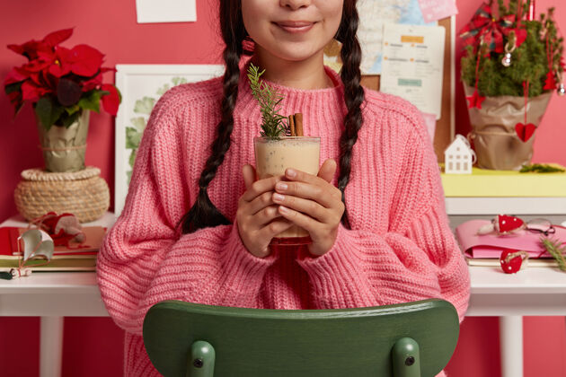 工作区小女孩穿着大号针织毛衣 手里拿着装满辛纳蒙的蛋奶酒 用云杉装饰 靠着桌面坐在椅子上 准备庆祝圣诞节手作物圣诞节