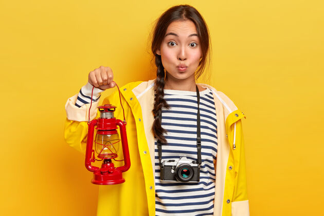 露营可爱的亚洲女人 留着黑色长发 手持红色火炬 穿着休闲的黄色雨衣和条纹套头衫 是一名活跃的游客 在夏天徒步旅行 用复古相机捕捉瞬间年轻人穿站