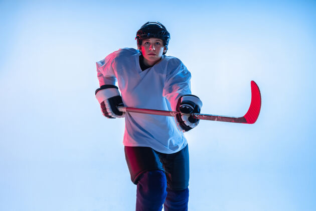 单独年轻人年轻的男性冰球运动员 在霓虹灯下用棍子粘在白墙上运动员戴着设备和头盔练习运动的概念 健康的生活方式 运动 运动 动作运动员冰运动
