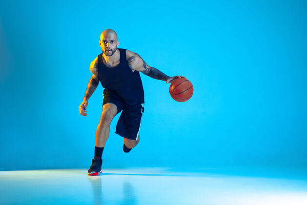 球员年轻的篮球队员穿着运动服训练 在运动中练习 运动在霓虹灯下隔离在蓝色的墙上运动的概念 运动 活力和活力 健康的生活方式动态举行强壮