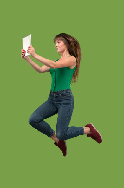 女性年轻女子跳过绿色工作室使用笔记本电脑或平板电脑小玩意 而跳跃成功成人运动