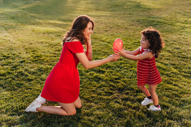 童年一个穿着红裙子的可爱女人和她的女儿在公园里玩耍一张笑着的年轻女士微笑着看着小妹妹的户外照片快乐孩子户外