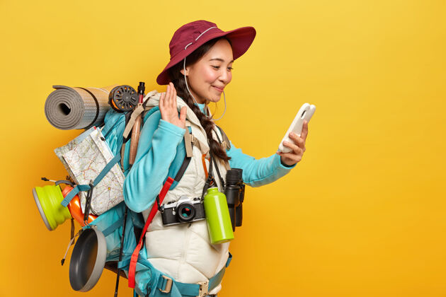 人漂亮的黑发女人打视频电话 用手掌在智能手机摄像头前挥手 在探险中使用现代科技与朋友保持联系旅游现代旅行者