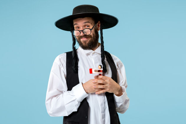 男性一位年轻的东正教犹太男子在普赖姆节期间手持木制棘轮的画像帽子庆典节日