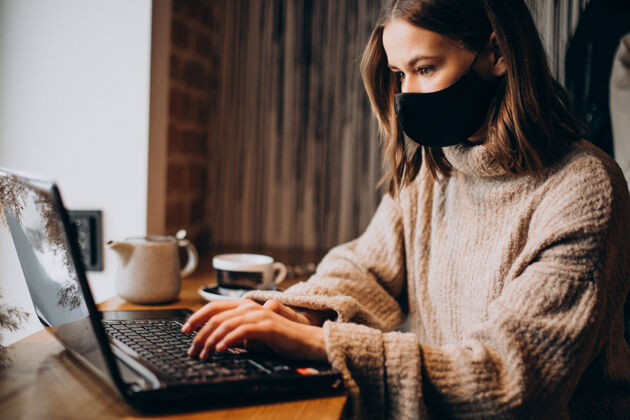 女戴着面具在咖啡馆里用笔记本电脑工作的年轻女子人微笑互联网