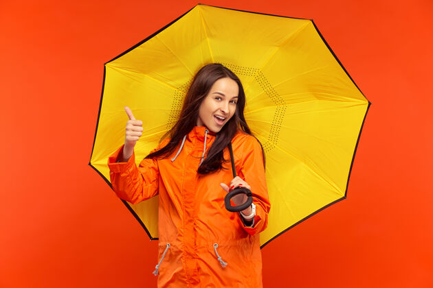 下雨一个快乐的微笑着的小女孩穿着秋天的橘色夹克在摄影棚里摆姿势成人女性保护