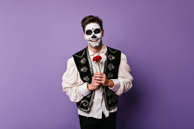 骷髅穿着白衬衫的快乐僵尸男子与花合影室内照片是一个快乐的高加索人和红玫瑰服装多彩僵尸
