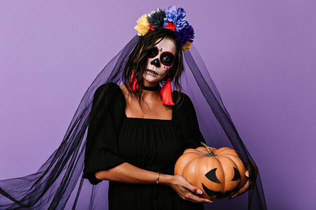 僵尸身穿黑色新娘服的女人手里拿着南瓜淡紫色墙上头发上插着花的女孩的画像墨西哥恐怖传统