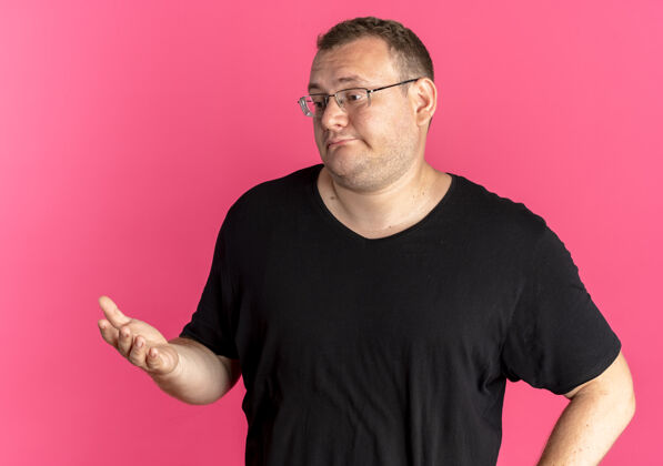 眼镜一个戴眼镜的胖男人 穿着黑色t恤 站在粉红色的墙上 一边看一边伸出胳膊思考或询问问手臂放一边