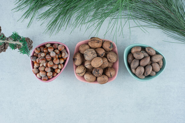 盘子三个装满坚果的小盘子 大理石背景上有圣诞松果高质量的照片坚果小健康