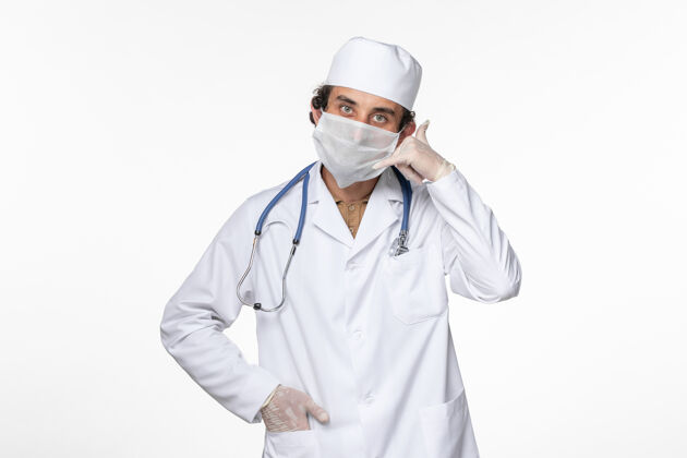 男性正面图身穿医疗服的男医生戴着无菌口罩 以防感染冠状病毒 在白色办公桌上摆出电话姿势电话正面视图