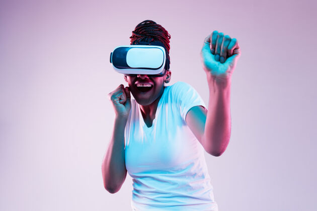 美国年轻的非洲裔美国妇女的肖像玩在虚拟现实眼镜在霓虹灯梯度背景现代情感周末