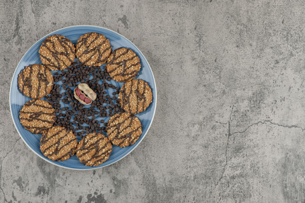 食品蓝色的饼干盘 巧克力和花生滴在大理石背景上美味坚果燕麦片