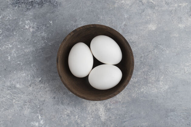 木头在大理石背景上放满新鲜白色鸡蛋的木碗午餐家禽食品