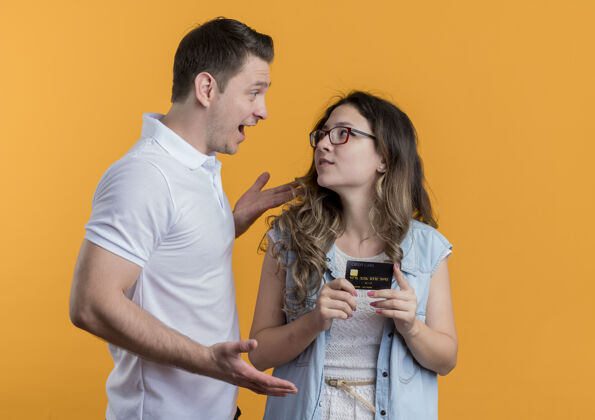 休闲一对穿着休闲服的年轻夫妇站在橙色的墙上和他微笑的女友交谈情侣男人衣服