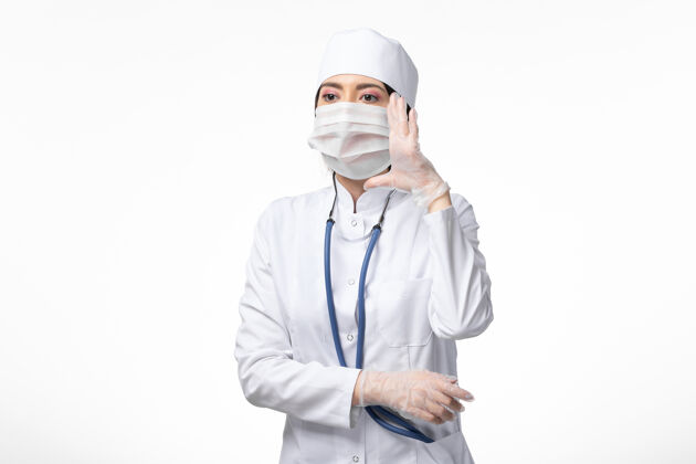 成人正面图女医生穿着白色医疗服 戴着口罩 因白墙上有冠状病毒病 医学病毒大流行 covid-专业正面病毒