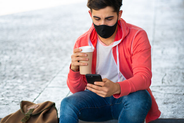 手机年轻人坐在街上用手机喝咖啡的照片戴着面具的男人城市概念电话无线小玩意