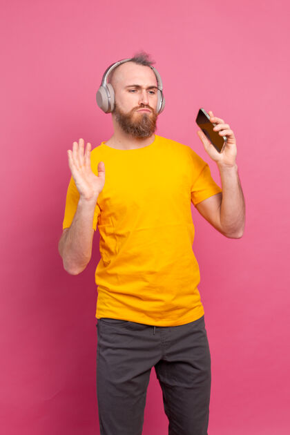 情感帅哥带着手机和耳机在粉色背景上翩翩起舞年轻耳机男性