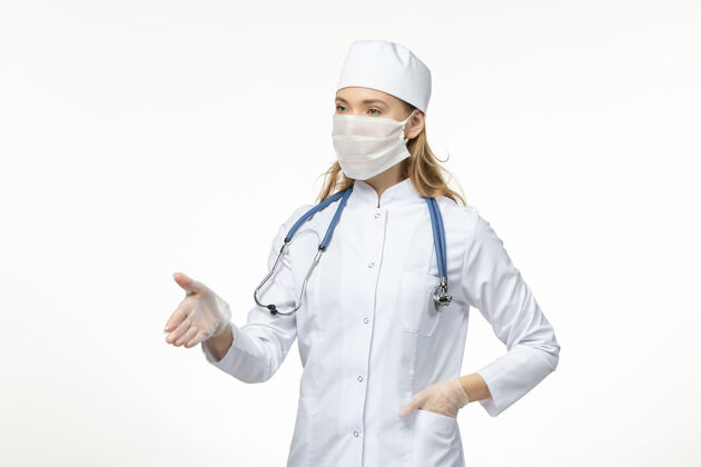 护士正面图女医生穿着医疗服戴着口罩和手套因冠状病毒在白墙上大流行冠状病毒病疾病面罩专业