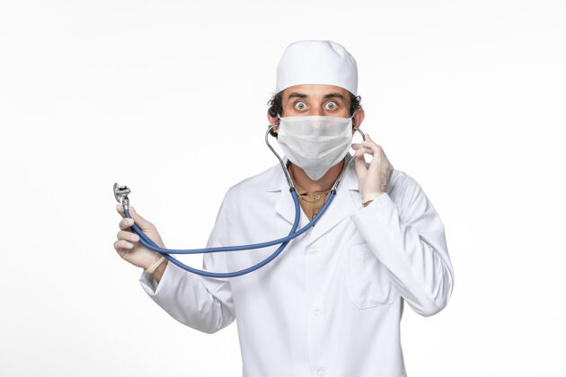 男性正面图：男医生穿着医疗服 戴着口罩以防感染冠状病毒-在白色桌面上使用听诊器飞溅冠状病毒大流行正面使用医疗