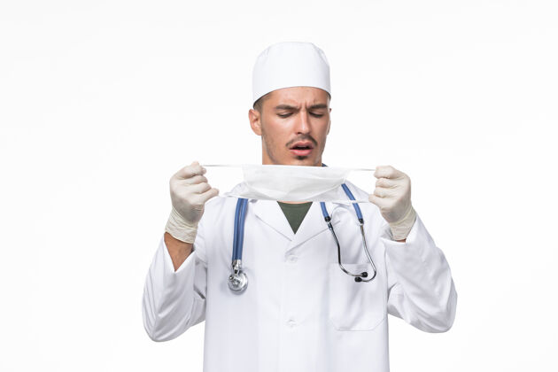 病毒正面图：男医生穿着医疗服 戴着防冠状病毒口罩 白色办公桌上病毒冠状病毒-疾病大流行防护专业人员听诊器