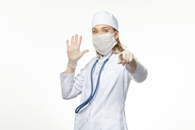 套装正面图：穿着白色医疗服 戴着白色口罩的女医生 在白色办公桌上抵御冠状病毒的侵袭视图女性人员