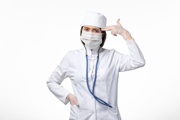 视图正面图女医生身穿白色无菌医疗服 带口罩 因白墙上冠状病毒病冠状病毒-大流行病毒实验室外套服装冠状病毒