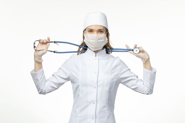 药品前视图女医生穿着医疗服戴口罩因冠状病毒手持听诊器白墙病毒大流行套装病毒视图