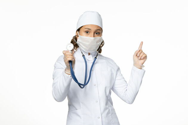 疾病正面图女医生穿着白色医疗服 戴着口罩 在白色办公桌上使用听诊器大流行病毒疾病药物视图女医院