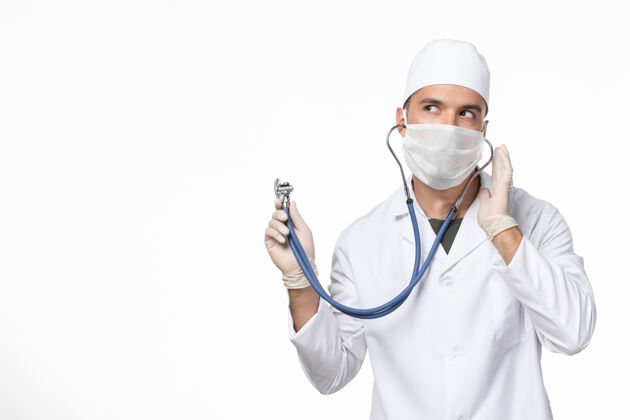 医疗正面图男医生穿着医疗服 戴着口罩因冠状病毒-使用听诊器对白墙冠状病毒-大流行病毒疾病外套穿着冠状病毒预防