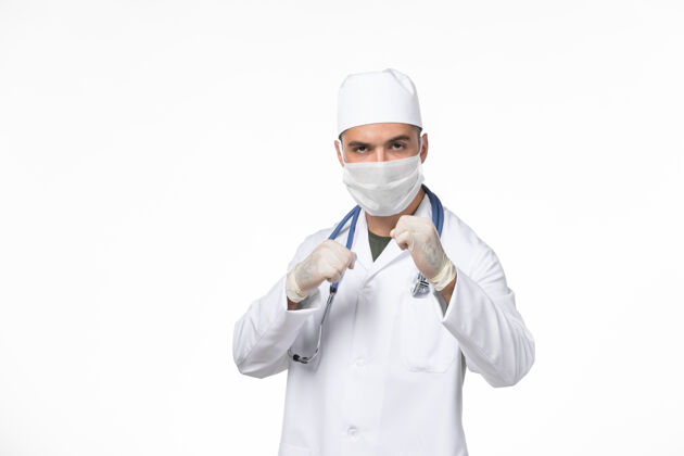 正面正面图：男医生穿着医疗服 戴着口罩 对抗白色墙壁上的冠状病毒-医学大流行疾病面具人医学