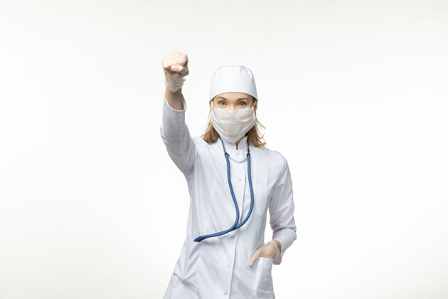 人正面图：穿着白色医疗服和面罩的女医生在白色办公桌上保护自己免受冠状病毒的侵害视图女性人