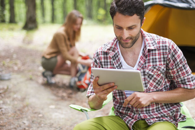 周末一对情侣在森林里露营男人在用数字平板电脑现代寻找度假