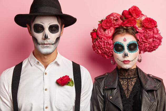 特写死亡幽灵夫妇一起庆祝万圣节 组织化妆舞会 穿着传统的墨西哥服装 生动的妆容 红花花环 在工作室摆姿势 肩并肩站着死亡之日死亡墨西哥传统